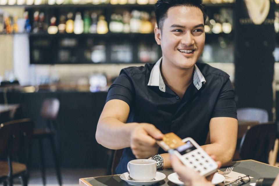 A person holding a credit card above a portable point-of-sale device while inside a restaurant.