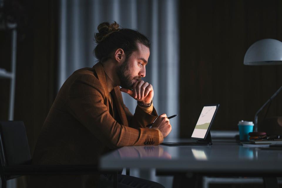 Person deep in thought while looking at graphs on a tablet computer.