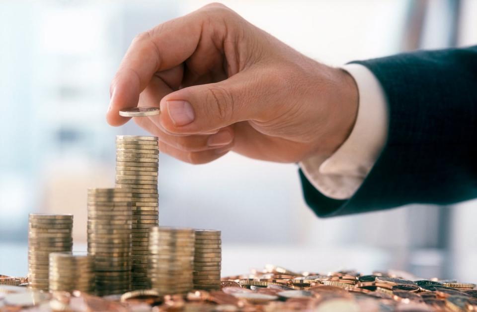 The arm and hand are visible of person wearing professional attire placing a coin onto a stack of other coins. 