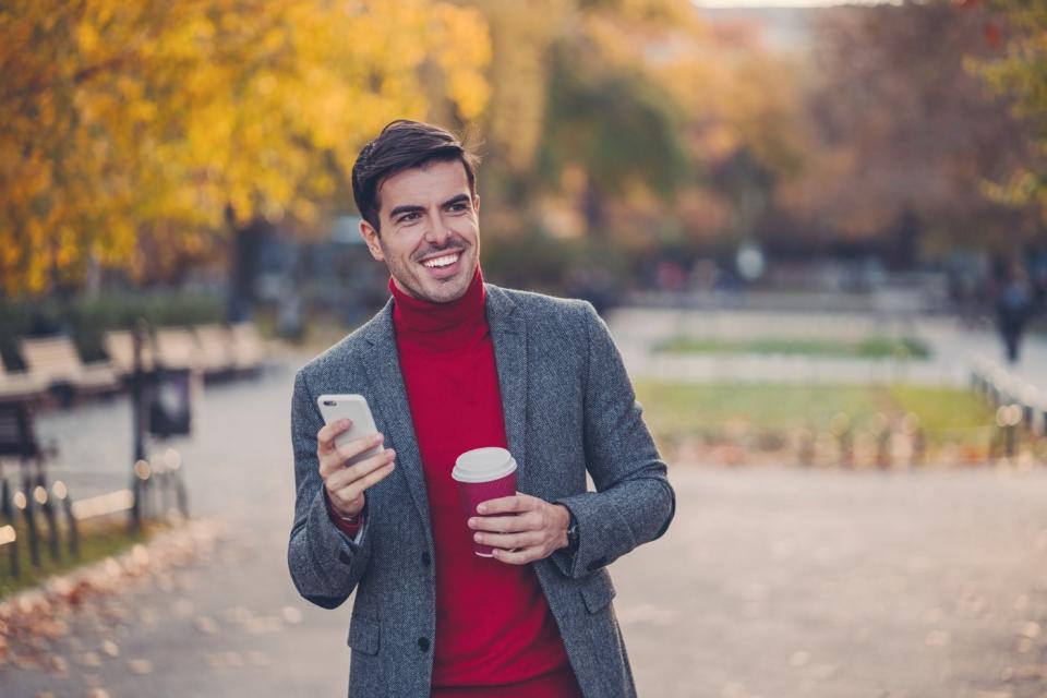 An investor smiles while walking through a park in the fall.